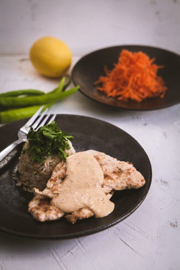 Brown rice and Chicken on a brown plate with shredded carrots in the background