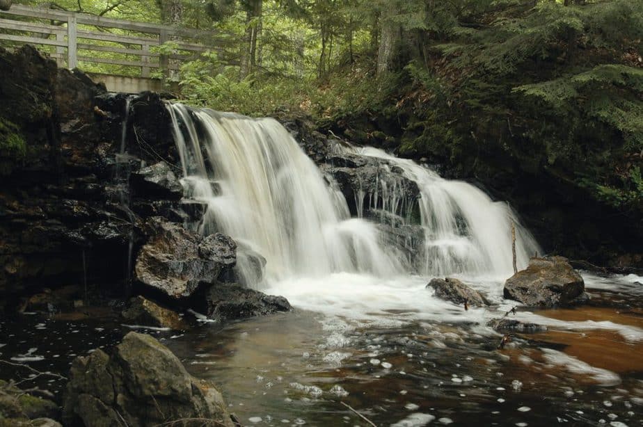 A waterfall with a wooden bridge and a trees in the background. 