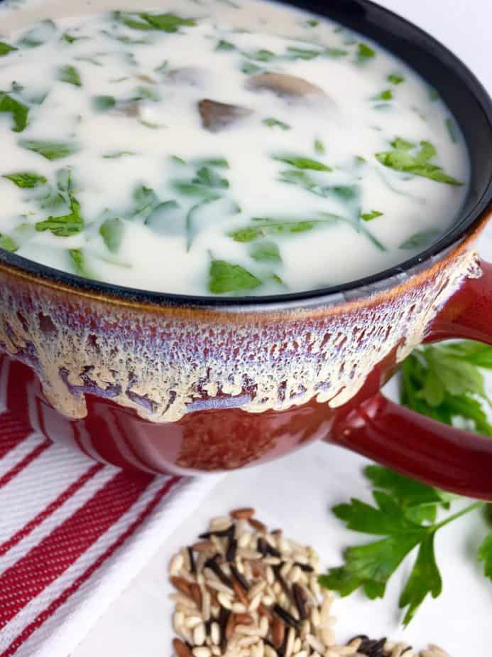 Wild rice soup in a red bowl with wild rice on the table next to it.