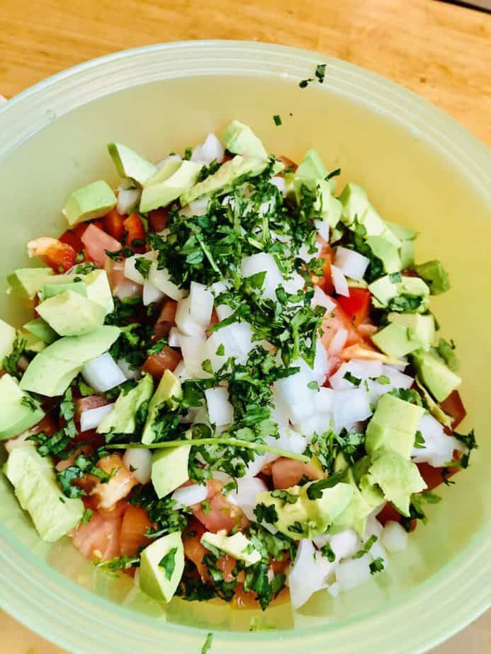 chopped up tomatoes, avocado, onions, peppers and chickpeas in a green bowl with cilantro on top