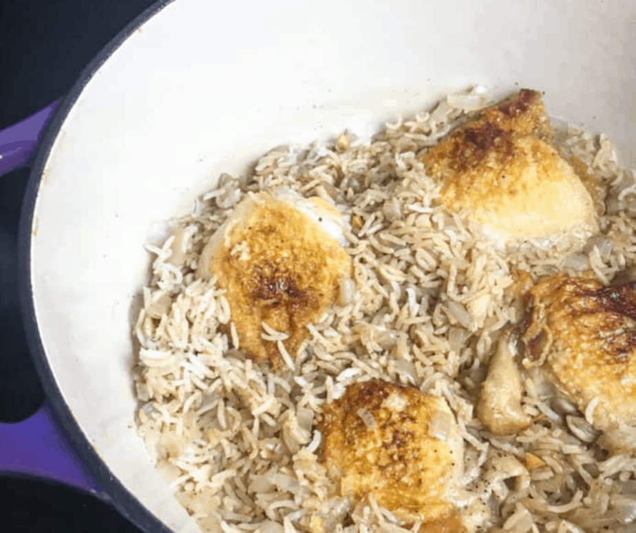 Dutch oven with wild rice and chicken thighs. The chicken thighs have been seared, so their skin is brown and crispy.