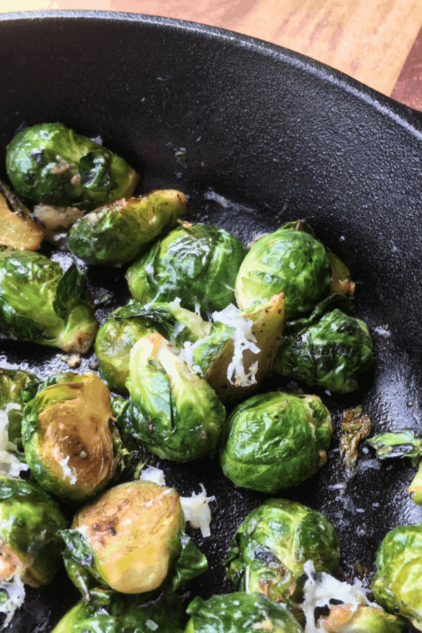 A cast-iron pan, filled with lightly browned Brussels sprouts lightly dusted with shredded cheese. 