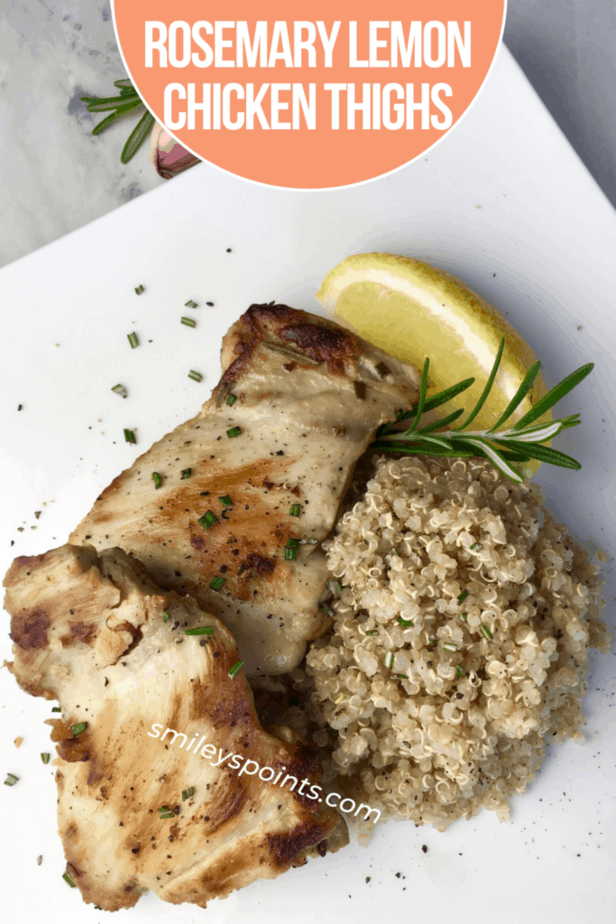 A nicely browned chicken thigh sits on a white plate. To the right is a pile of rice, on top of the rice and chicken is a sprig of rosemary and a lemon wedge. 