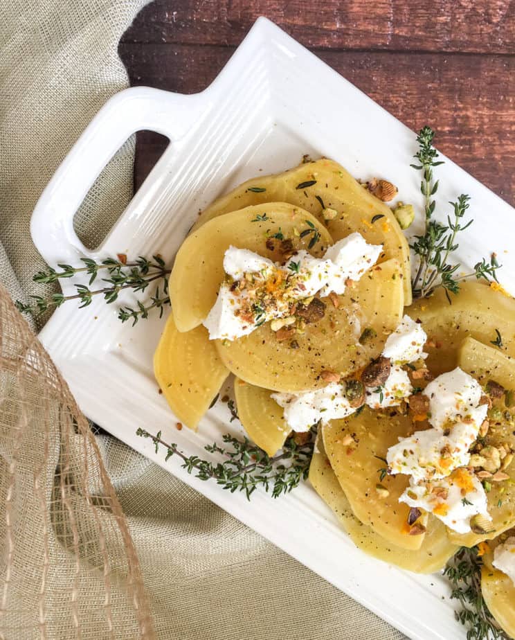 Golden Beets arranged on a white platter garnished with thyme and pistachios