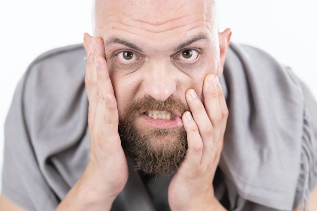 TMJ Don't clench your teeth. Man with a beard with his hands on his face teeth clenched.