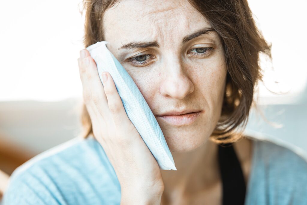 TMJ pain. Picture of a woman holding an ice pack to her jaw.