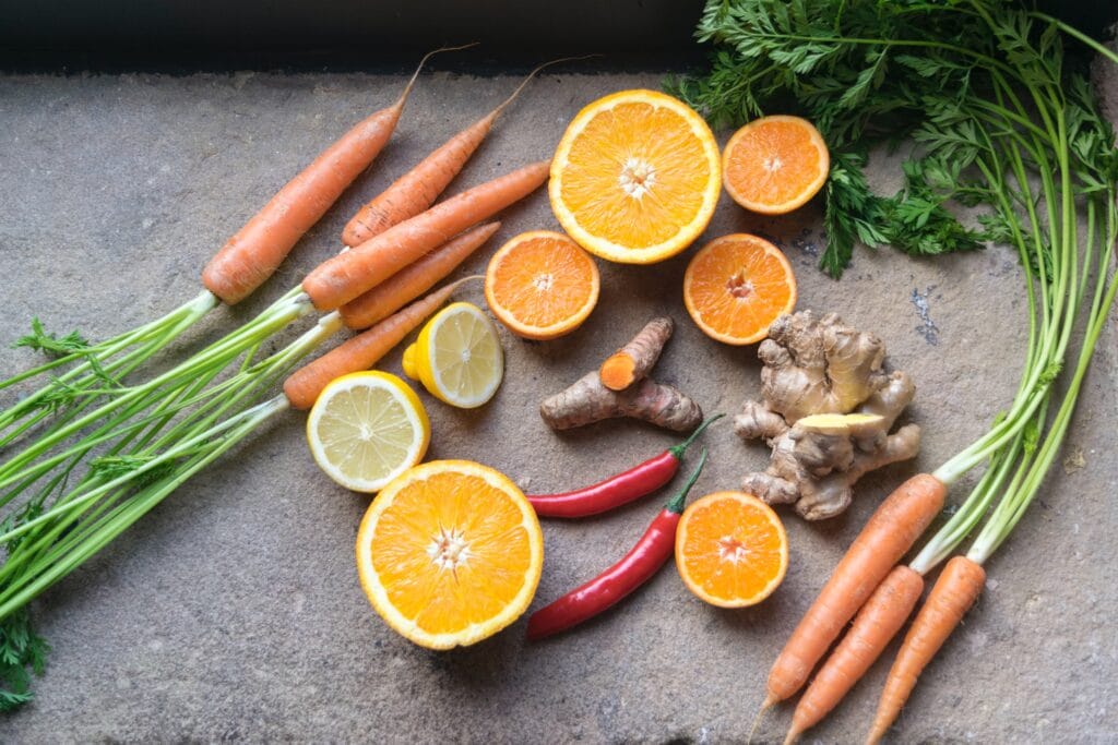 A table with carrots, ginger roots, lemons halved, oranges halved, and chili peppers