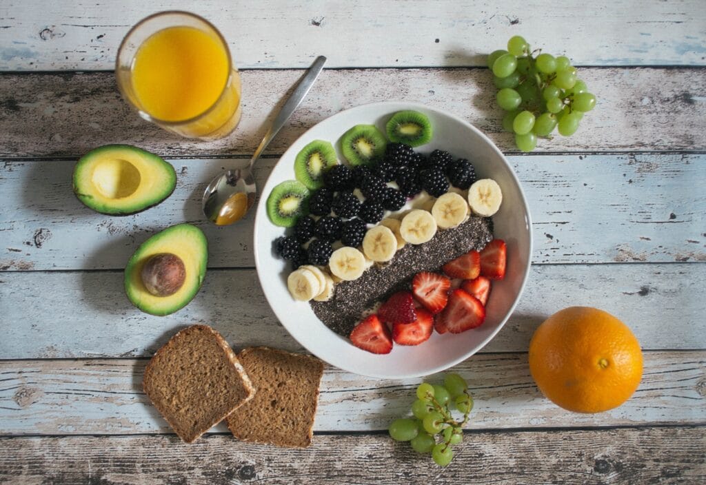 A white bowl with various fruits and vegetables in it on a wood table