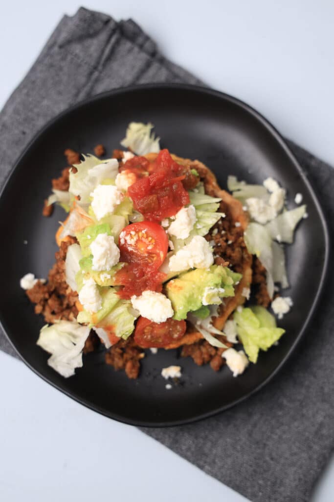 sope on a black plate topped with avocado, tomatoes, ground beef, and cheese