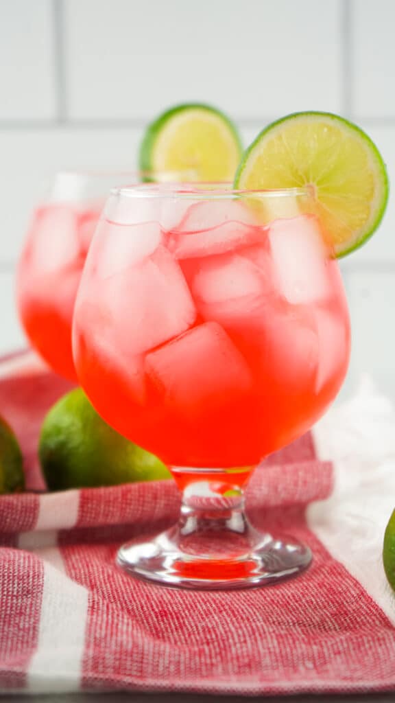 A red liquid in a glass with a slice of lime on the rim. Dirty Shirley Cocktail in a glass sitting on a red towel.