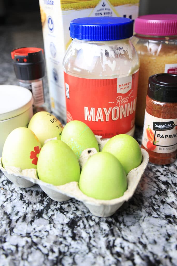 Easter eggs dyed lime green, mayonnaise, paprika, garlic on a black and white counter