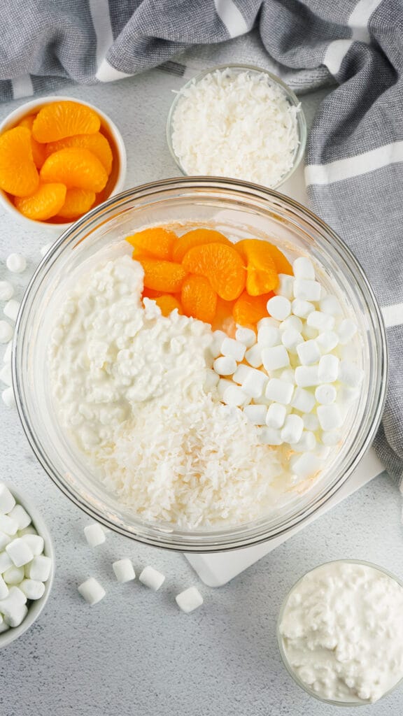 Orange fluff mixed in a bowl. shredded coconut and mandarin oranges in bowls on the side