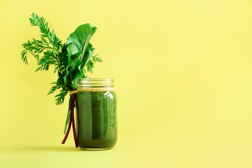 Smoothie with beet greens and carrot tops on yellow background, copy space. Summer vegan food concept. Healthy detox eating, alkaline diet. Fresh squeezed juice, drink from vegetables. Leafy greens